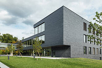 Auf dem Bild ist ein Gebäude mit dunkelgrauen Schieferschindeln an der Fassade zu sehen. Auf dem Bild ist ein Gebäude mit dunkelgrauen Schieferschindeln an der Fassade zu sehen.