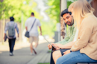 Studierende unterhalten sich, mit Blick auf den Laptop. Sie sitzen im Außenbereich des Campusteil Burren. Studierende unterhalten sich, mit Blick auf den Laptop. Sie sitzen im Außenbereich des Campusteil Burren.