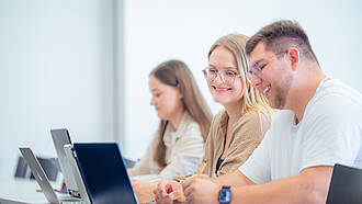 Drei Studierende sitzen im Hörsaal vor ihren Laptops. Drei Studierende sitzen im Hörsaal vor ihren Laptops.