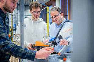 F-Titelbild Studierende aus dem Bachelorstudiengang Mechatronik arbeiten mit einem Professor an einem Roboterarm.